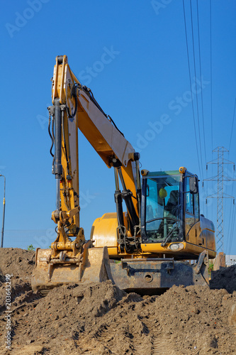 Yellow Excavator on the ground and electric lines on the blue sky