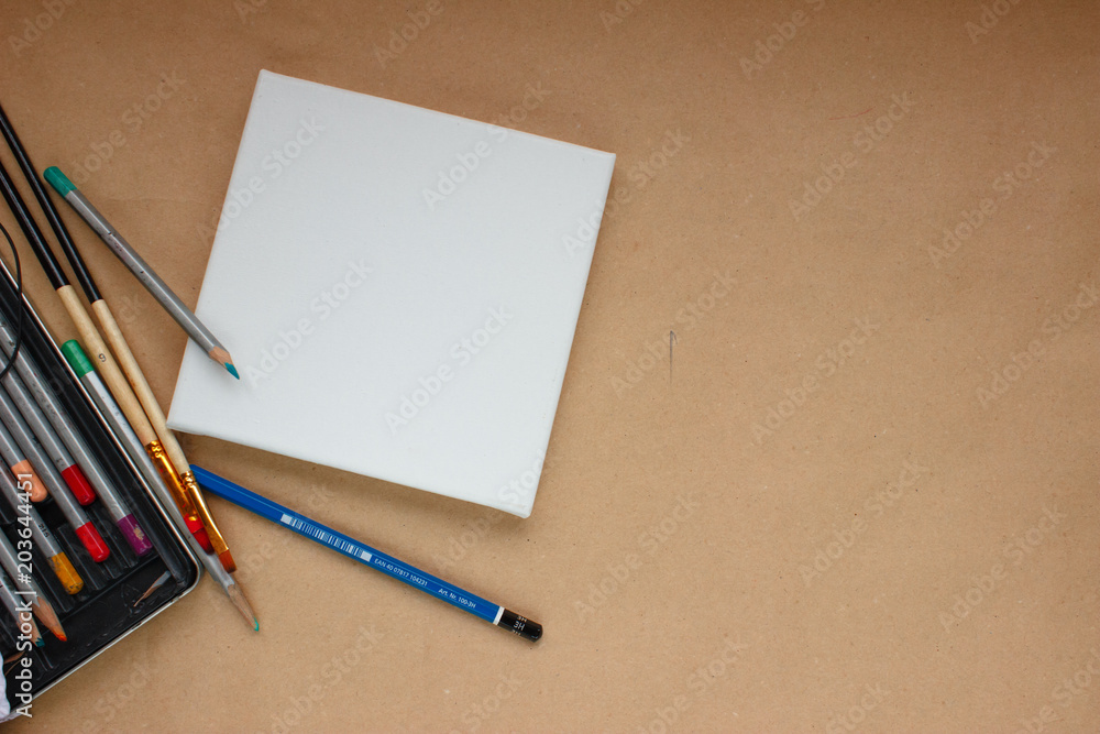 Blank canvas on craft paper background with pencils and brushes copy space Blank canvas on craft paper background with pencils and brushes copy space