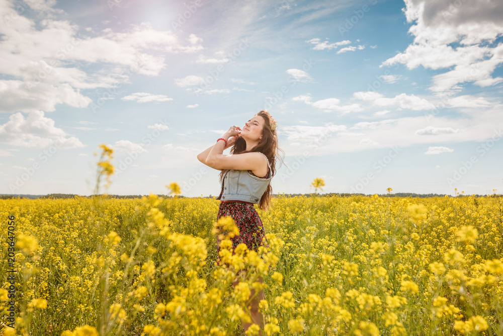 Young beautiful girl with a flower wreath in her hair enjoys the sunshine on a yellow field. Young beautiful girl with a flower wreath in her hair enjoys the sunshine on a yellow field.