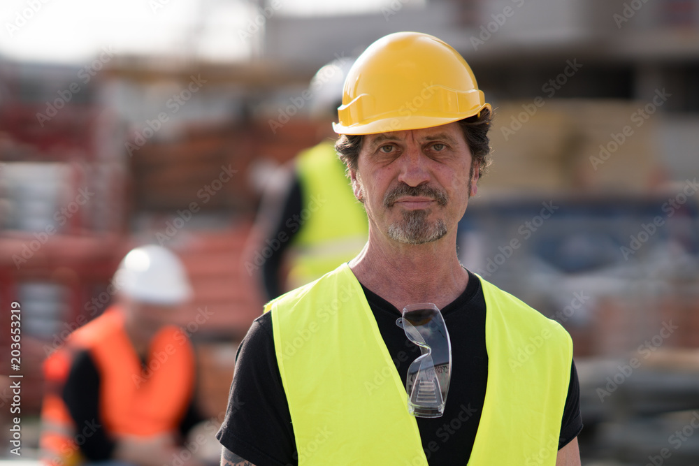 Portrait of a caucasian civil engineer wearing yellow reflective jacket and hardhat posing looking at the camera Portrait of a caucasian civil engineer wearing yellow reflective jacket and hardhat posing looking at the camera