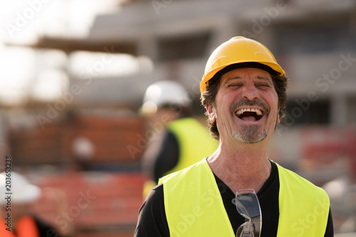 Front view portrait of a caucasian civil engineer wearing yellow reflective jacket and hardhat laughing looking at the camera