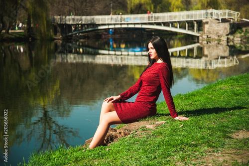  beautiful young brunette with long hair in a park on a spring in spring among flowering trees in a red dress in hands holds magnolia flowers