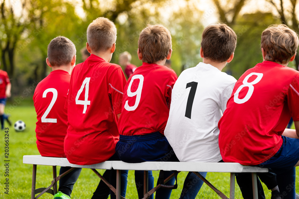 Fototapeta premium Kids Soccer Team Players Sitting on a Bench on a Sunny Day. Children Football Team Players. Young Boys Watching Soccer Match. Youth Footballers of Soccer Academy. Football School Tournament