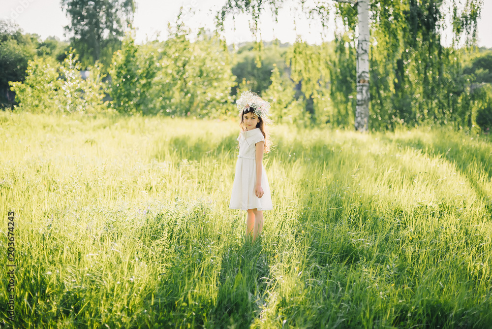 girl in a white dress with a wreath on her head on a meadow in nature on a Sunny summer day