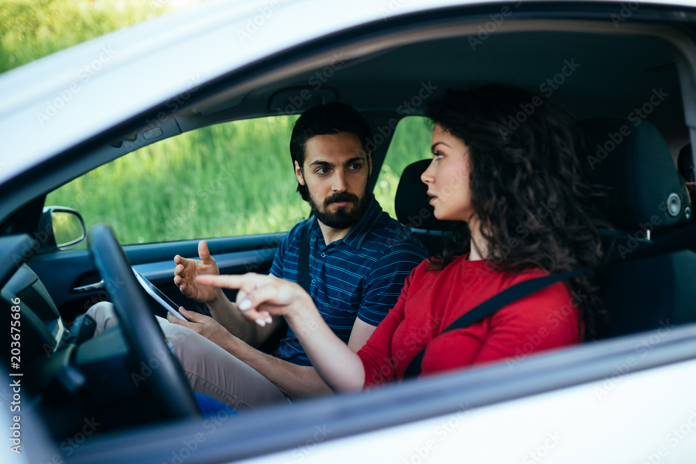 Obraz premium Driving school or test. Beautiful young woman learning how to drive car together with her instructor.