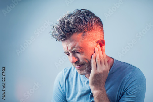 male having ear pain touching his painful head isolated on gray background photo