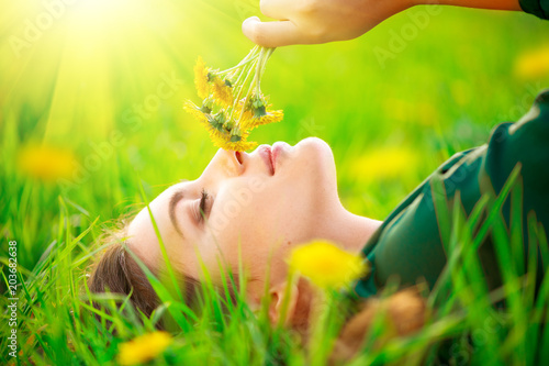Εκτύπωση καμβά Beautiful young woman lying on the field in green grass and smelling blooming dandelions