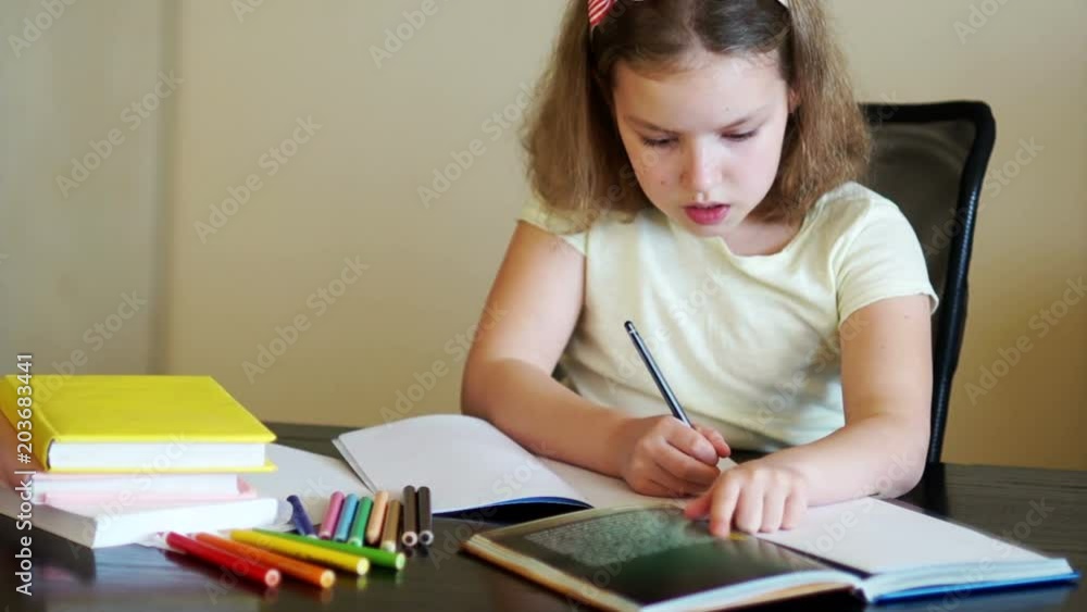 The schoolgirl does the homework. On the table are textbooks, exercise books and pencils. Back to school. Preparation for lessons. Homework. Day of Knowledge The schoolgirl does the homework. On the table are textbooks, exercise books and pencils. Back to school. Preparation for lessons. Homework. Day of Knowledge