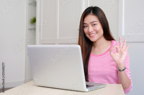 Young asian businesswoman showing okay hand gesture sign and smiling with happiness at home office desk, woman working in casual home office lifestyle concept