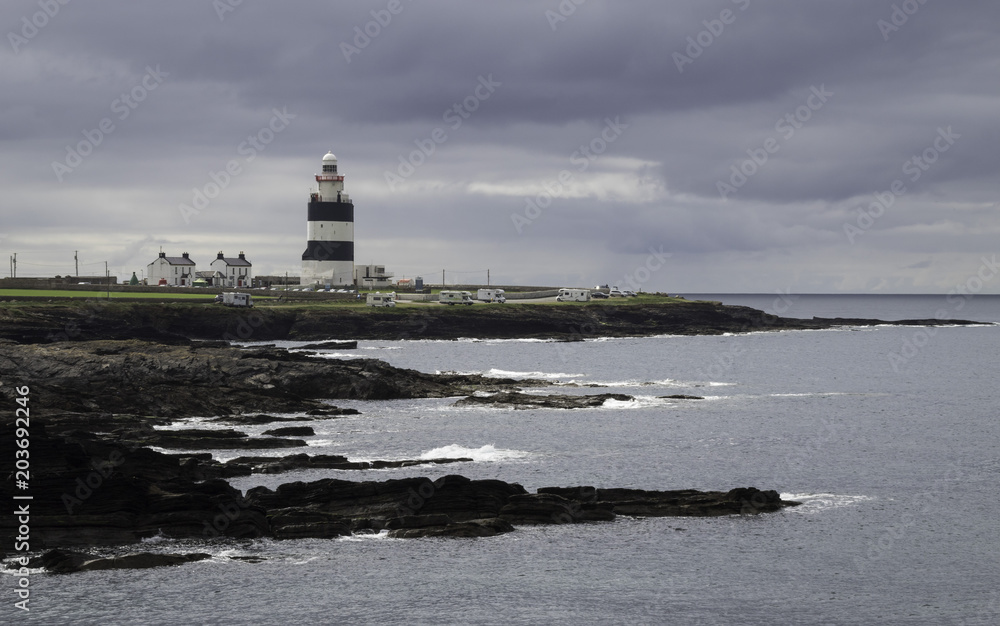 Navy and White Stripy Lighthouse Building with Rocky Coastline, Stormy Overcast Sky, Daylight Navy and White Stripy Lighthouse Building with Rocky Coastline, Stormy Overcast Sky, Daylight