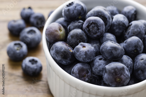 Small White Bowl filled with Blueberries, six blueberries on the left side, wooden background