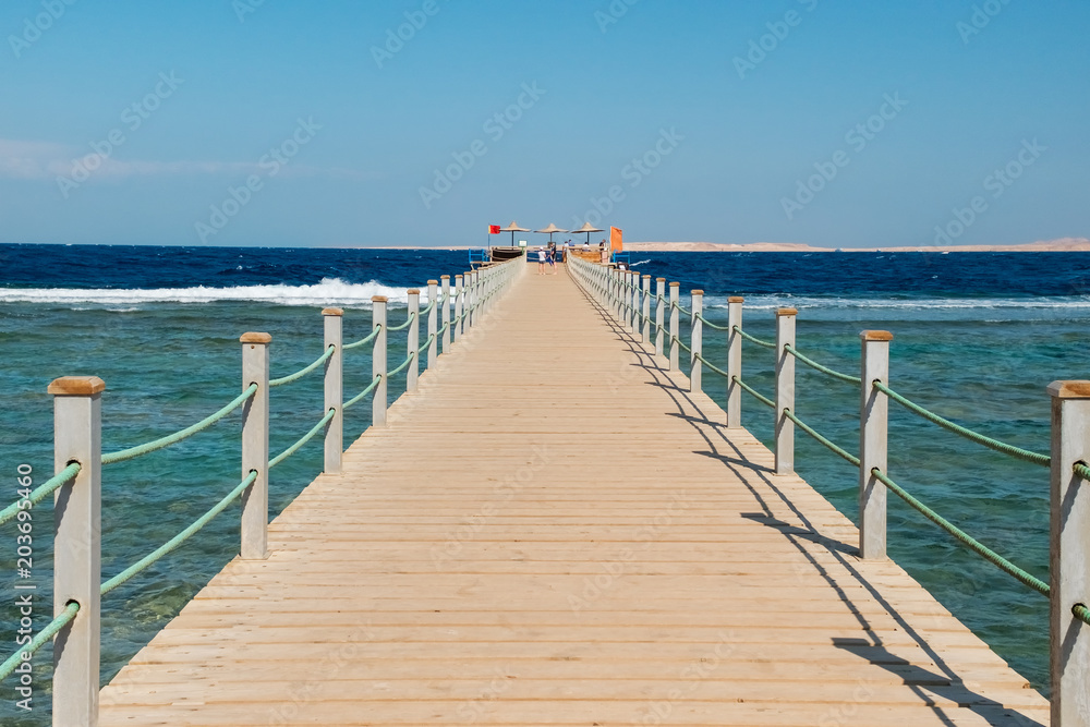 View of a wooden pier on the tropical seashore with blue sky and sea. View of a wooden pier on the tropical seashore with blue sky and sea.