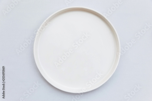 Top view of white empty plate on white tablecloth.