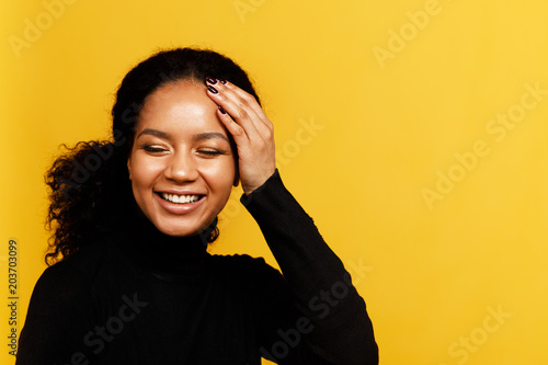 Young happy woman posing over yellow background with hand near head © Artem Varnitsin