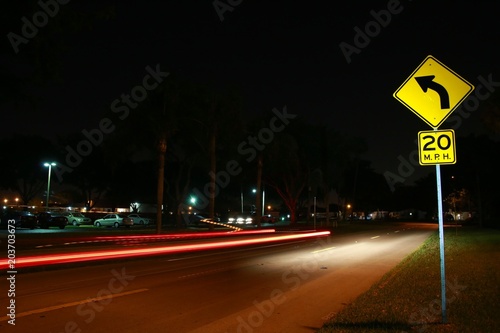 Yellow Speed Limit 20 Mph Sign in a Residential Neighborhood at Night with Car Lights Streaking by in a Long Time Exposure photo