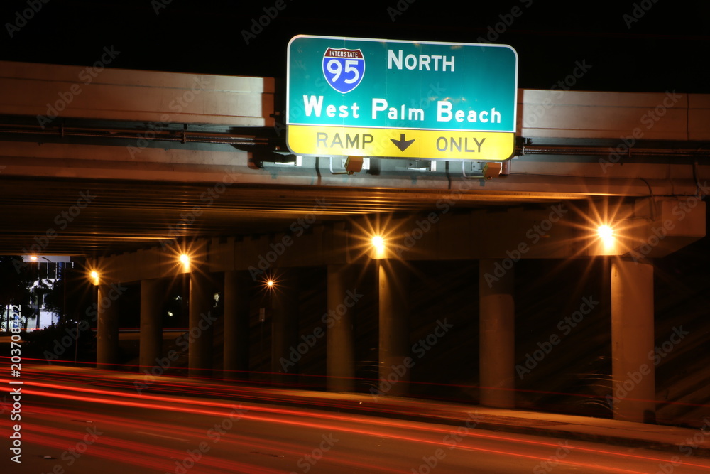 95 North to West Palm Beach Sign at Sample Road in Pompano Beach, Florida and the On-Ramp Under the Overpass at Night with Car Tail Lights Streaking in a Long Time Exposure