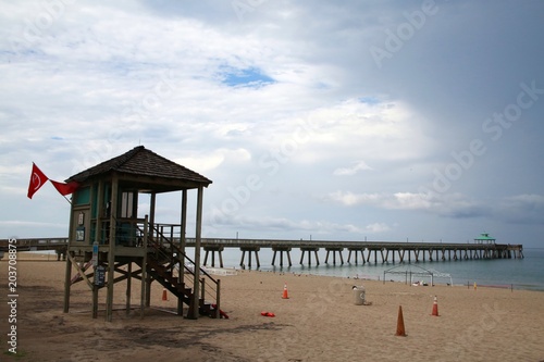 Lifeguard Station with Colored Flags and Cones in the Sand Overlooking Deerfield Beach, Florida Pier under Cloudy Sky Before a Rain