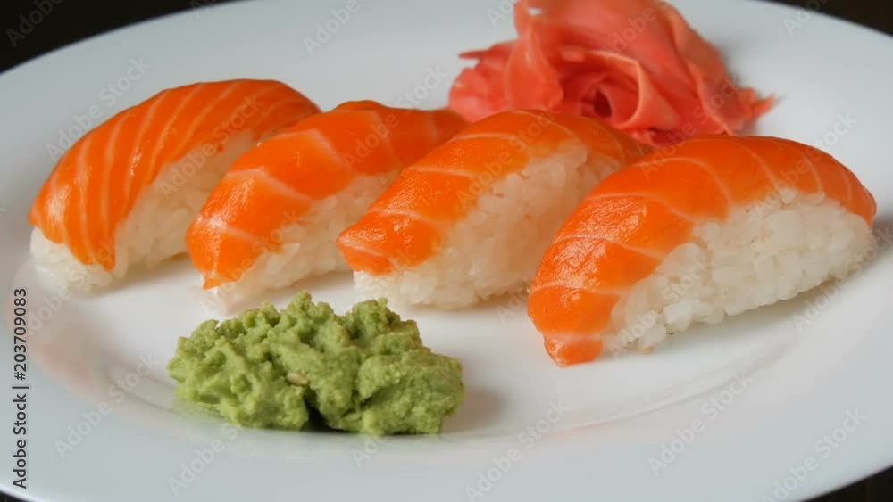 Four large sushi with piece of salmon lie on a large flat plate. Four large sushi with piece of salmon lie on a large flat plate.