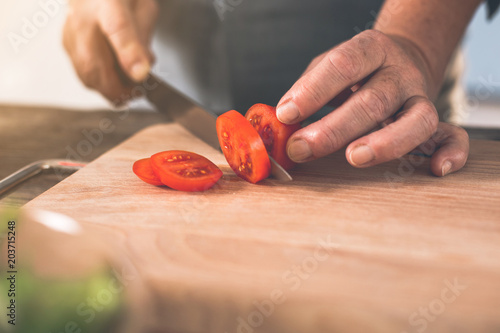 Close up of old woman hands cutting a tomato on wooden board. Healthy food preparation concept
