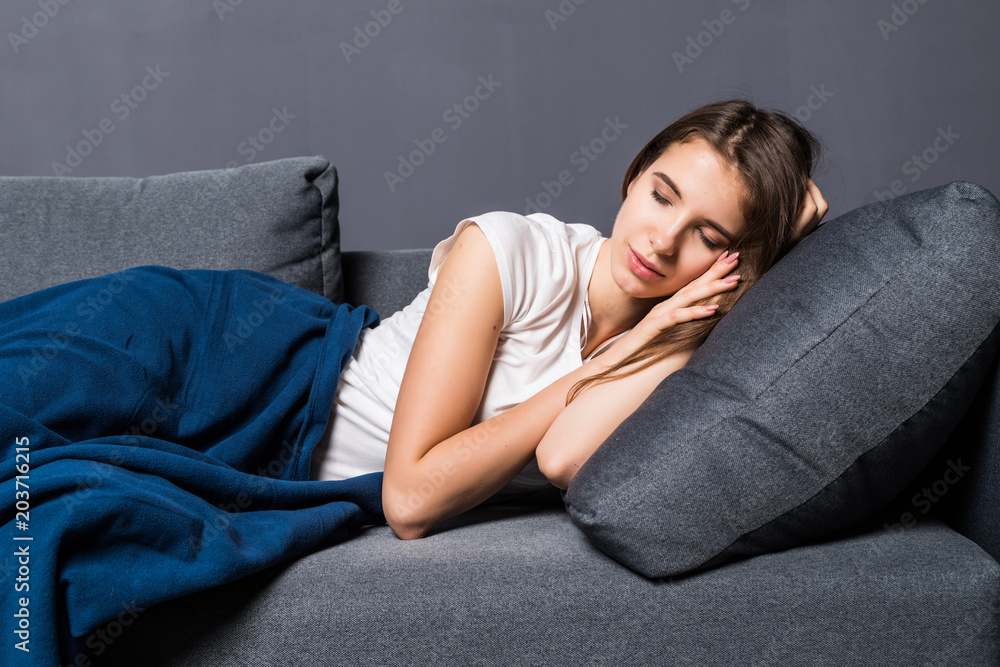 Portrait of a young cute girl sleeping on the sofa in light livingroom. Her head is on grey pillow and she is covered with beige blanket Portrait of a young cute girl sleeping on the sofa in light livingroom. Her head is on grey pillow and she is covered with beige blanket