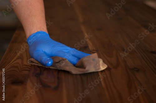Woodwork oil being applied on wood . Blue rubber gloves are used.