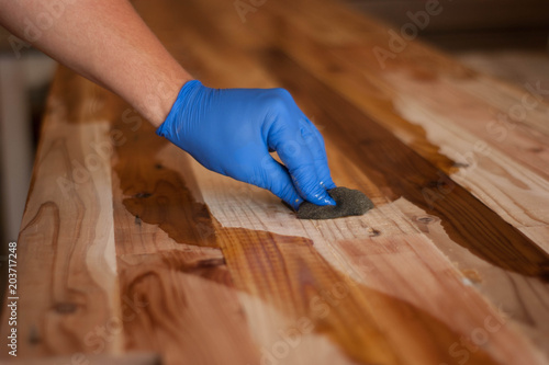 Woodwork oil being applied on wood . Blue rubber gloves are used.