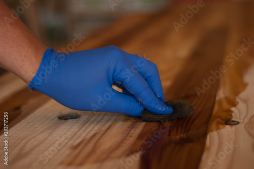 Woodwork oil being applied on wood . Blue rubber gloves are used.