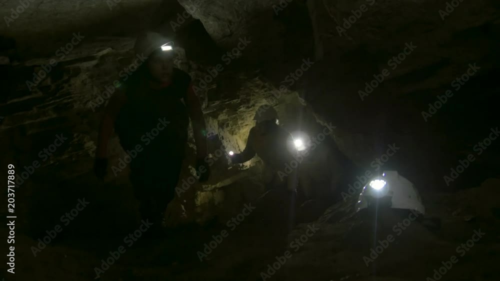 Group of young speleologists climb up in the dark narrow cave Group of young speleologists climb up in the dark narrow cave