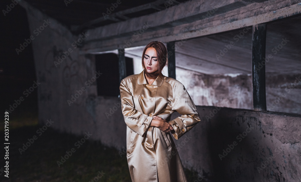Abstract photo of a beautiful young woman in a beige silk coat against a background of concrete walls of an underground city station.