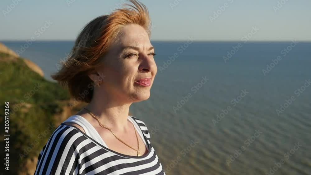 Profile of a cheerful blond woman in a striped navy blouse smiling happily and looking at the Black Sea on a sunny daay in summer in slow motion Profile of a cheerful blond woman in a striped navy blouse smiling happily and looking at the Black Sea on a sunny daay in summer in slow motion