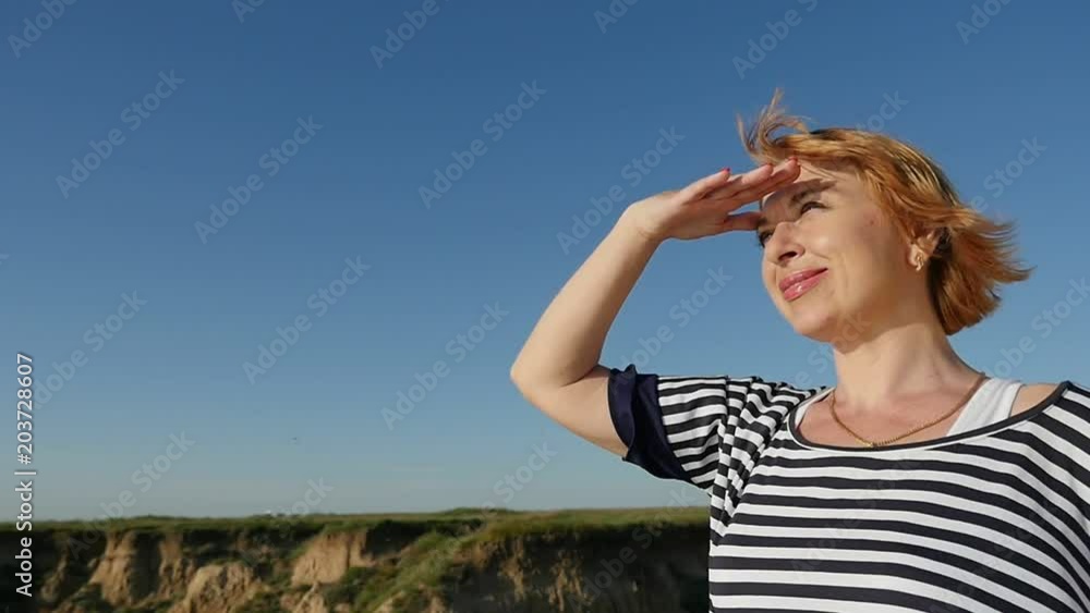 Profile of a cheery woman in a striped blouse looking away while keeping her hand over the eyes on thehilly Black Sea coast in summer in slo-mo Profile of a cheery woman in a striped blouse looking away while keeping her hand over the eyes on thehilly Black Sea coast in summer in slo-mo