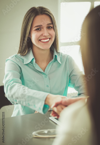 Two businesswomen sitting at a desk shaking hands photo