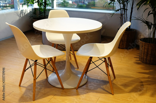 White round table and three comfortable chairs at the corner of the room with windows to the city view at two sides of the wall