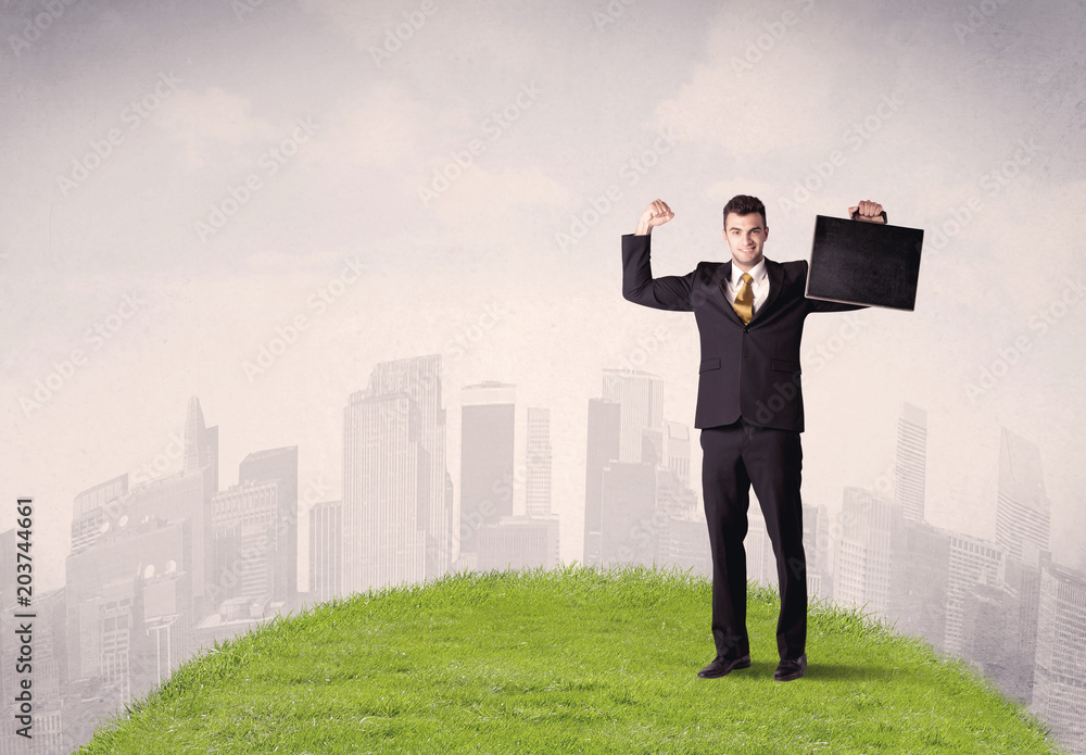 A confident male well looking office manager standing in small green grass in front of city landscape with tall buildings concept. A confident male well looking office manager standing in small green grass in front of city landscape with tall buildings concept.