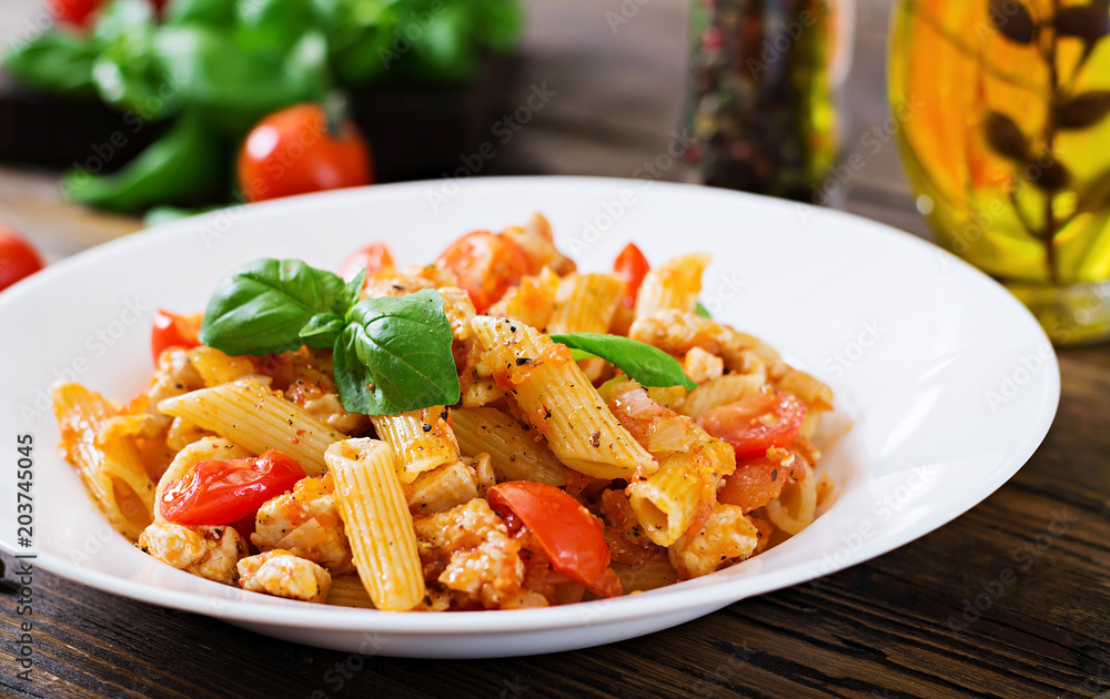 Penne pasta in tomato sauce with chicken, tomatoes, decorated with basil on a wooden table. Italian food. Pasta Bolognese. Penne pasta in tomato sauce with chicken, tomatoes, decorated with basil on a wooden table. Italian food. Pasta Bolognese.