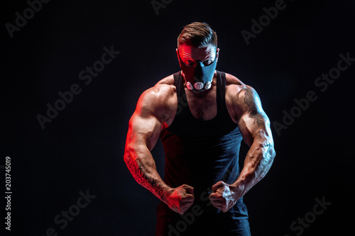 Strong male athlete in a black training mask posing on a black background photo