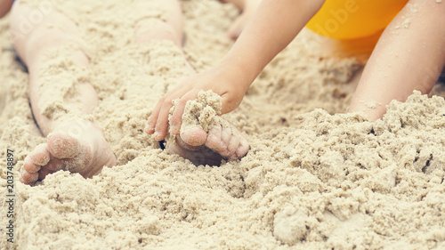 Children's feet are buried in sand. Happy holiday on th e sea coast.