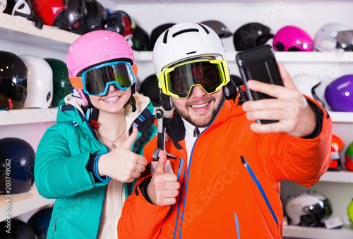 Happy couple in skiing equipment taking selfie during shopping