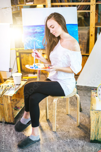 Young female student getting classes at art studio, learning how to draw seascapes, mixing different watercolors on pallet. photo