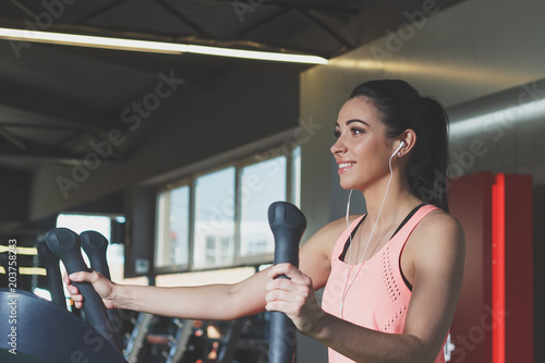 Sporty young woman makes sport exercises on the electrical trainer
