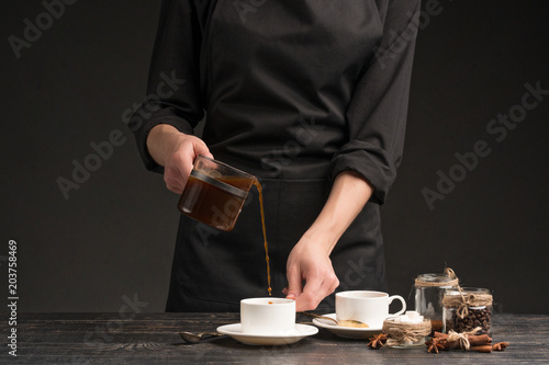 A professional barista pours coffee into a cup. Against a dark background