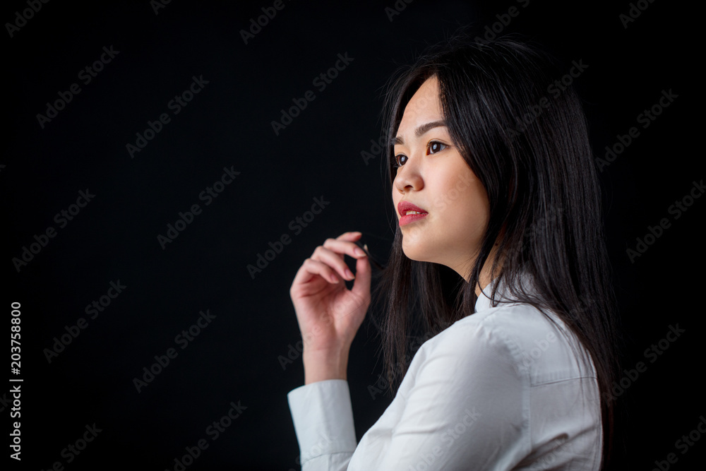 Asian pencive attractive woman in white shirt, profile view against studio black background Asian pencive attractive woman in white shirt, profile view against studio black background