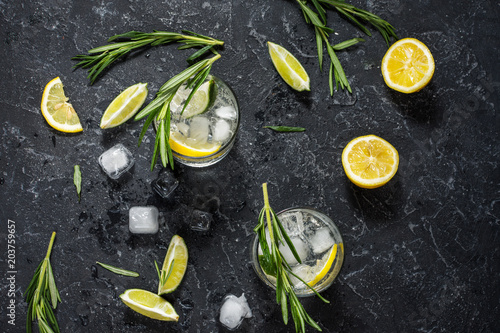 Alcoholic drink gin tonic cocktail with lemon, rosemary and ice on stone table