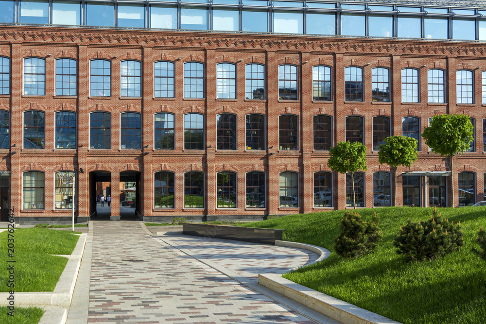 Office building of red brick in the courtyard of an old factory. Several trees and a lawn.