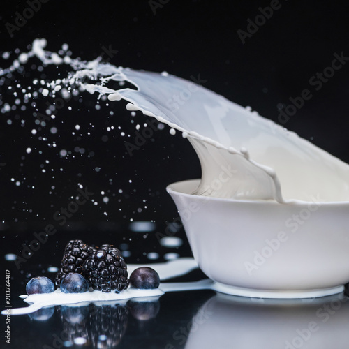 Ripe organic berries dropping in white bowl with milk on black background