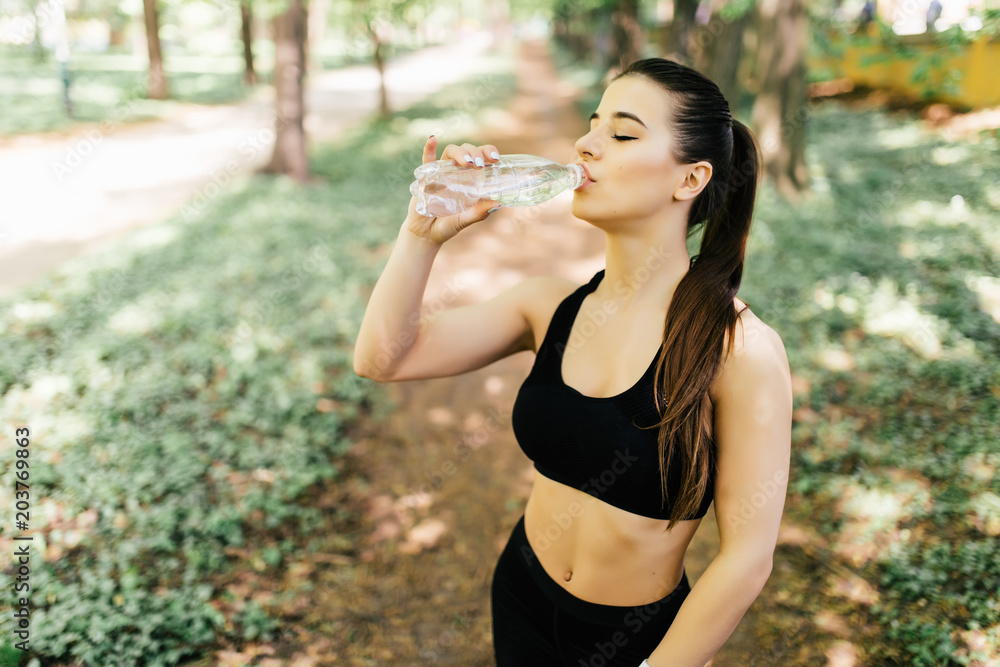 Beautiful sport athletic woman running in a park and drinking water Beautiful sport athletic woman running in a park and drinking water