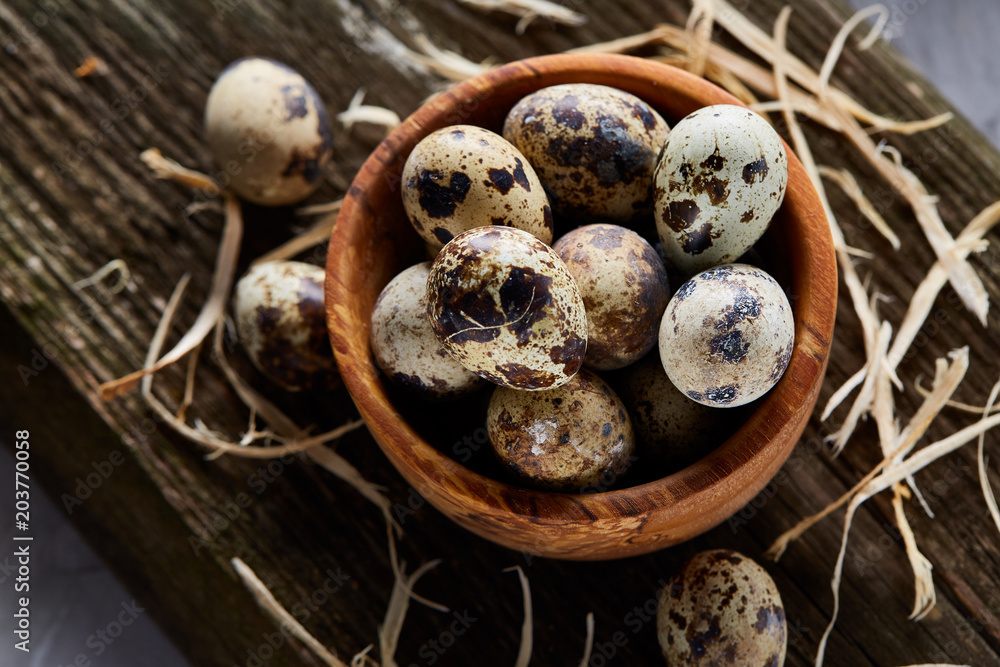 Wooden bowl filled with quail eggs on wooden board over white background, close-up, selective focus. Wooden bowl filled with quail eggs on wooden board over white background, close-up, selective focus.