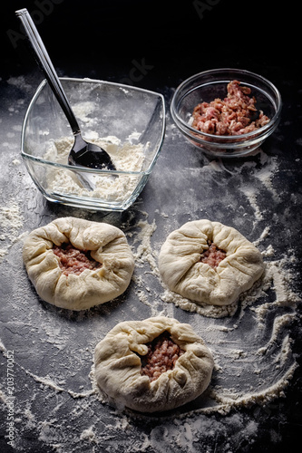 Pies with meat, potatoes and onions. Bowls with flour and tartar. The process of preparation on a black background. photo