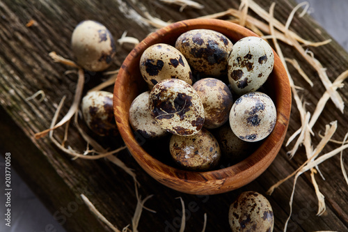 Wooden bowl filled with quail eggs on wooden board over white background, close-up, selective focus.