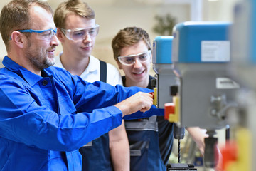 Group of young people in mechanical vocational training with teacher at drilling machine // Berufsausbildung - Jugendliche und Lehrer in der Berufsschule 
